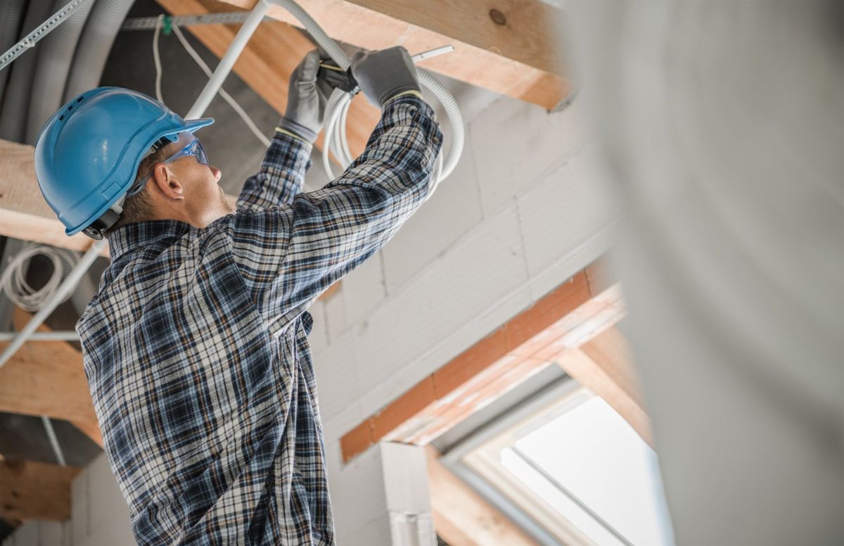 Electrician in a hard hat and safety glasses securing cable to roof framing during rough-in