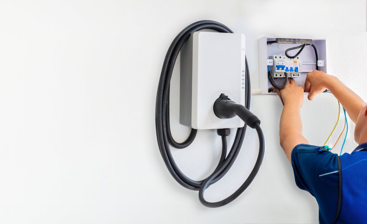 Electrician connecting a wall-mounted Level 2 EV charger to its circuit breaker enclosure