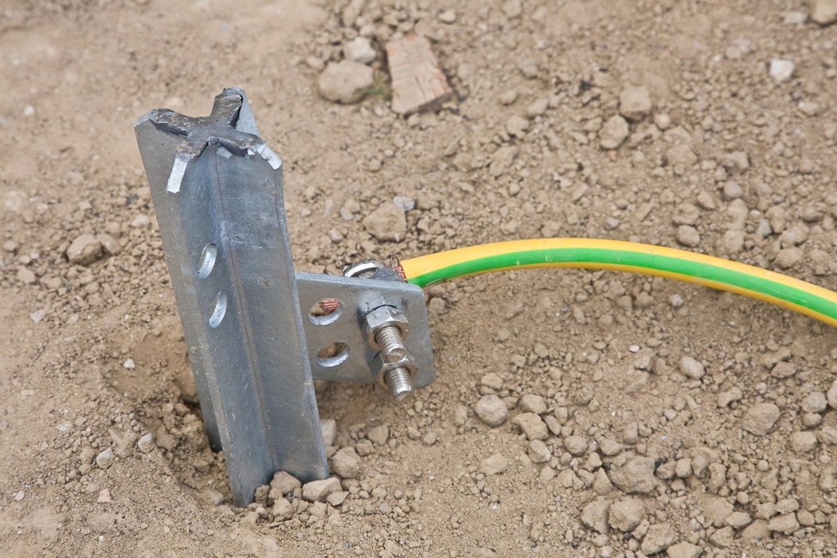 Grounding electrode driven into soil with a green and yellow grounding conductor bolted to it